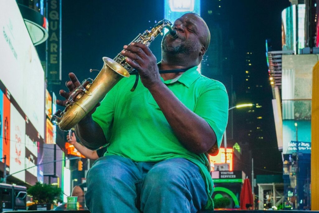 A man in a green shirt plays a saxophone in the vibrant setting of Times Square. Surrounded by bright billboards and city lights. Included: About BaoLiba – Transforming Influencer Marketing in Canada